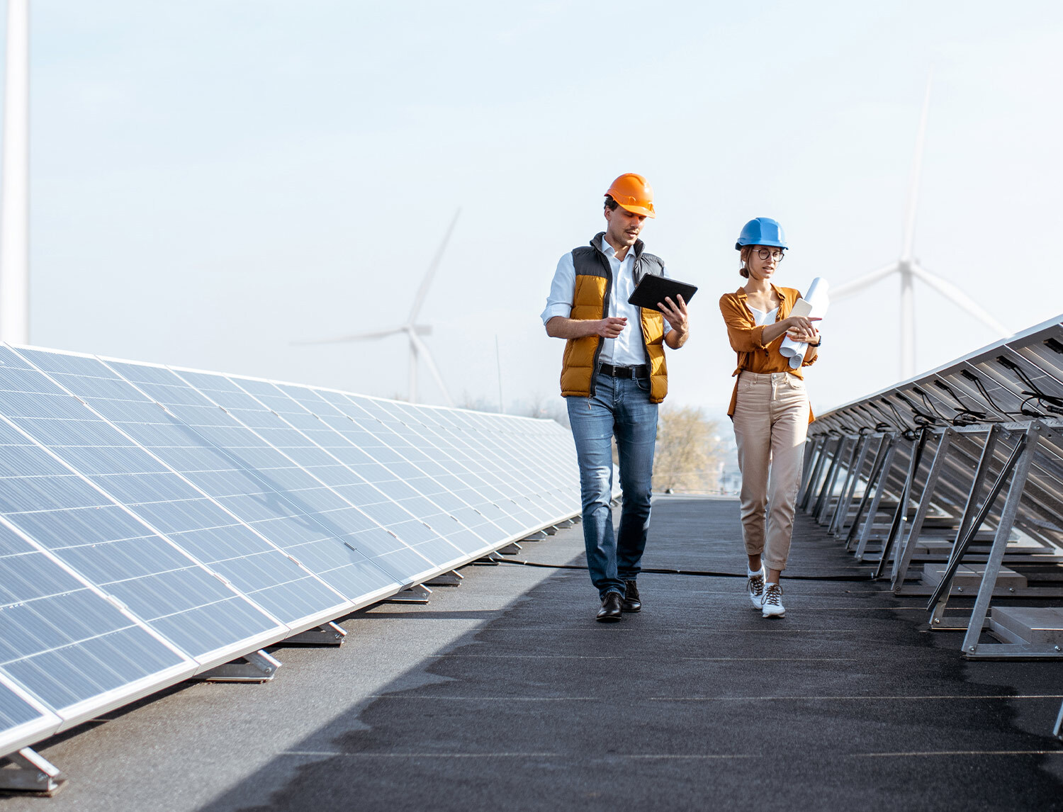A man and a woman wearing hard hats walking between two rows of solar panels