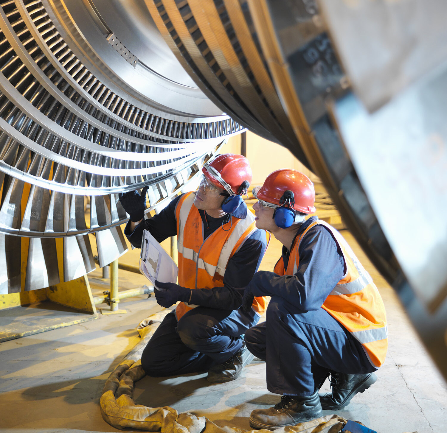 Two workers wearing safety gear inspecting a cargo ship engine component