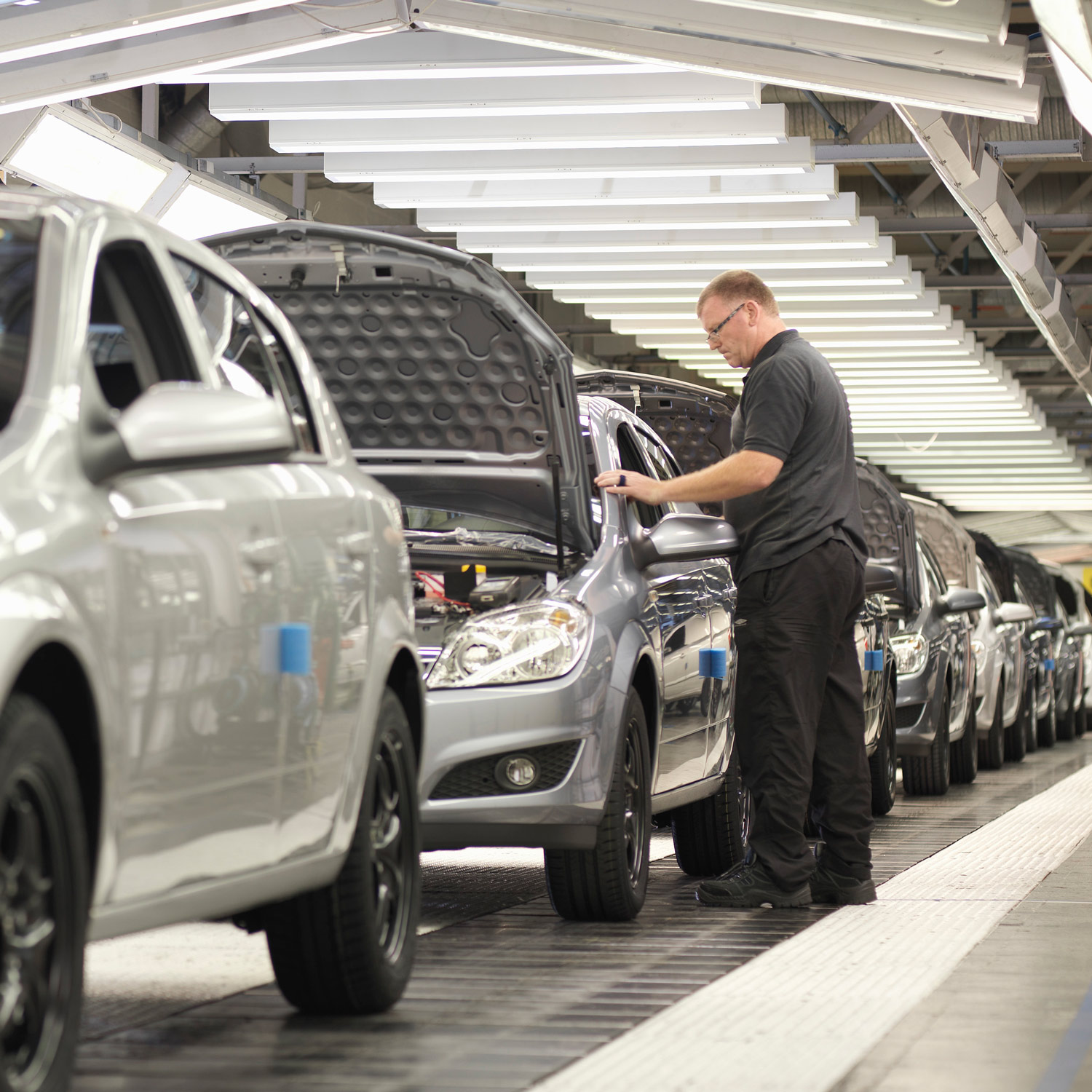 A man inspecting a line of silver cars at the end of an assembly line