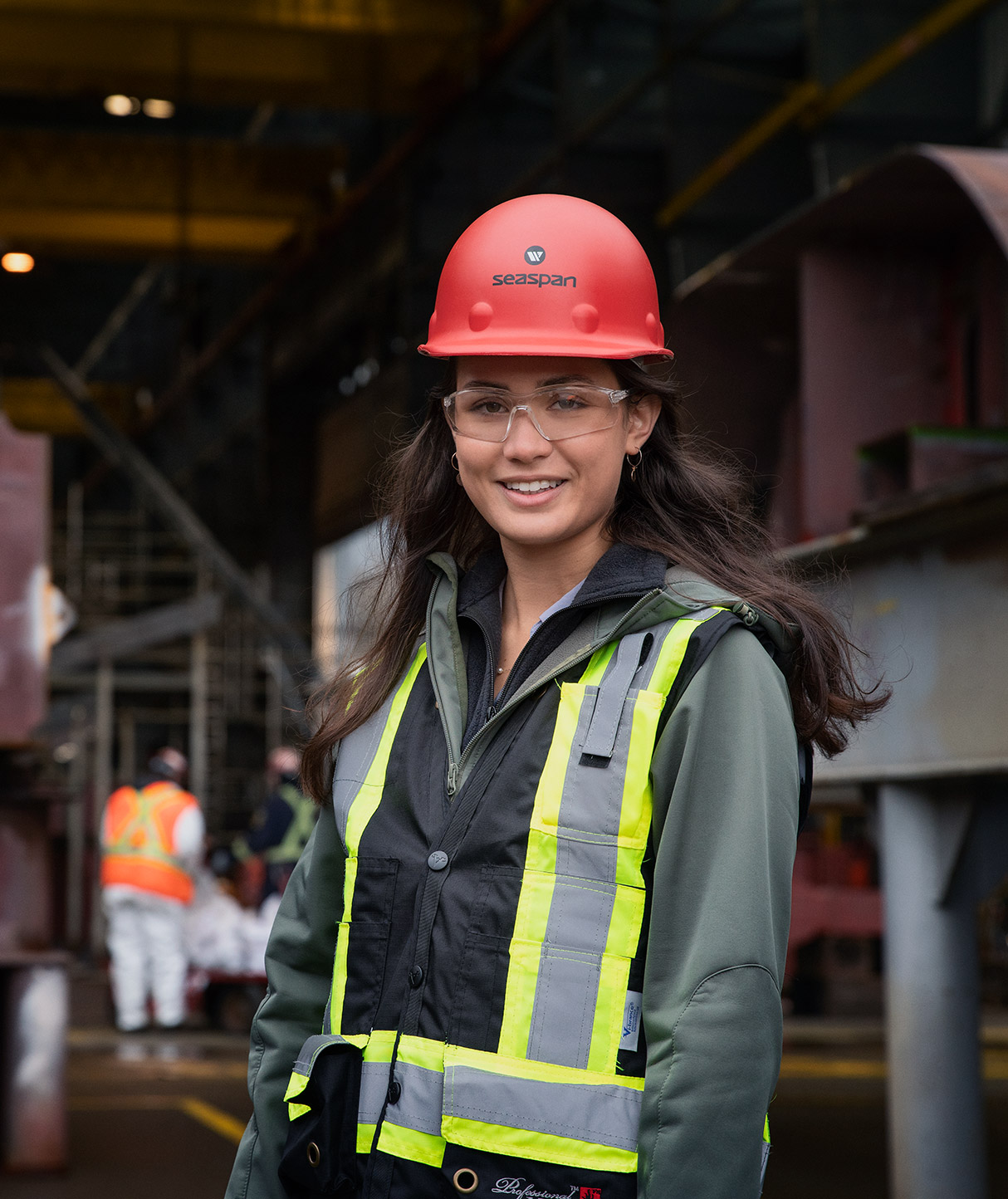 A portrait of a Female Seaspan employee wearing a red hard hat and a safety vest.